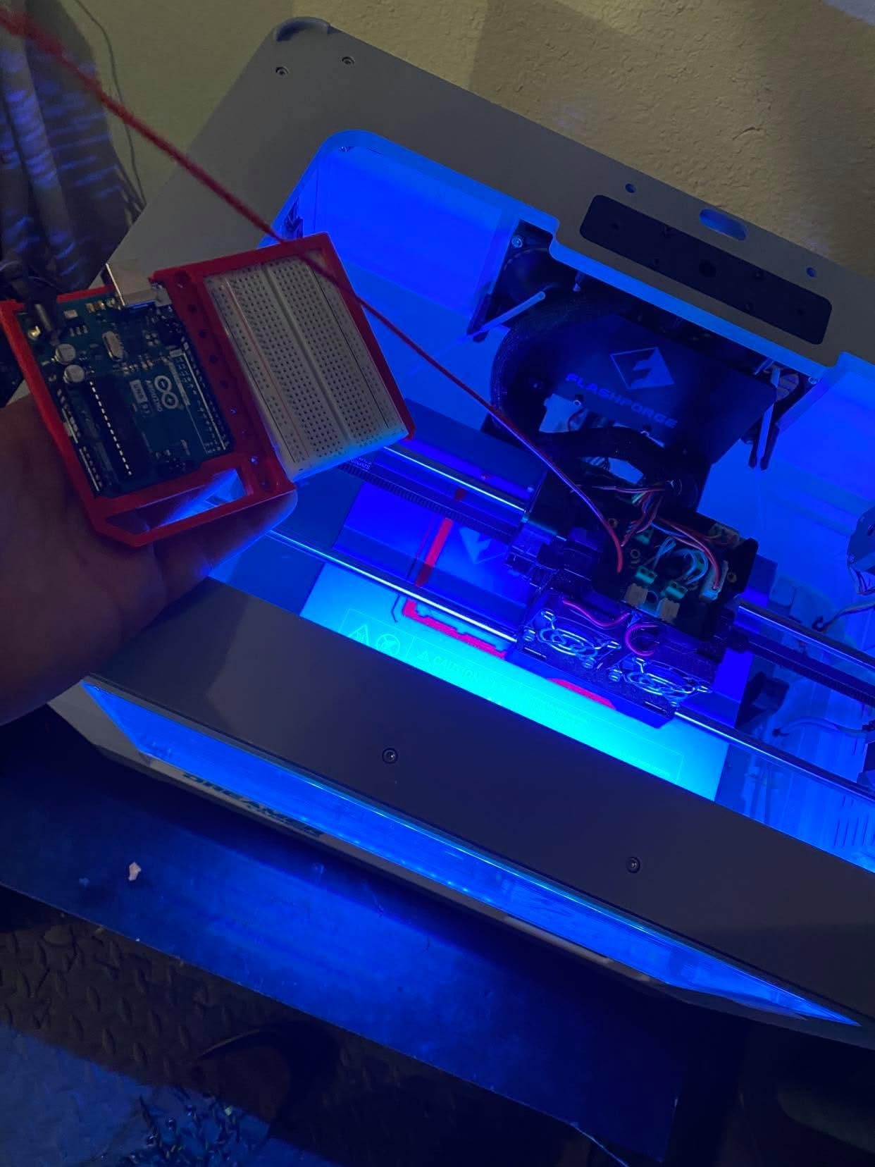Arduino electronics beside an illuminated 3D printer producing physical parts