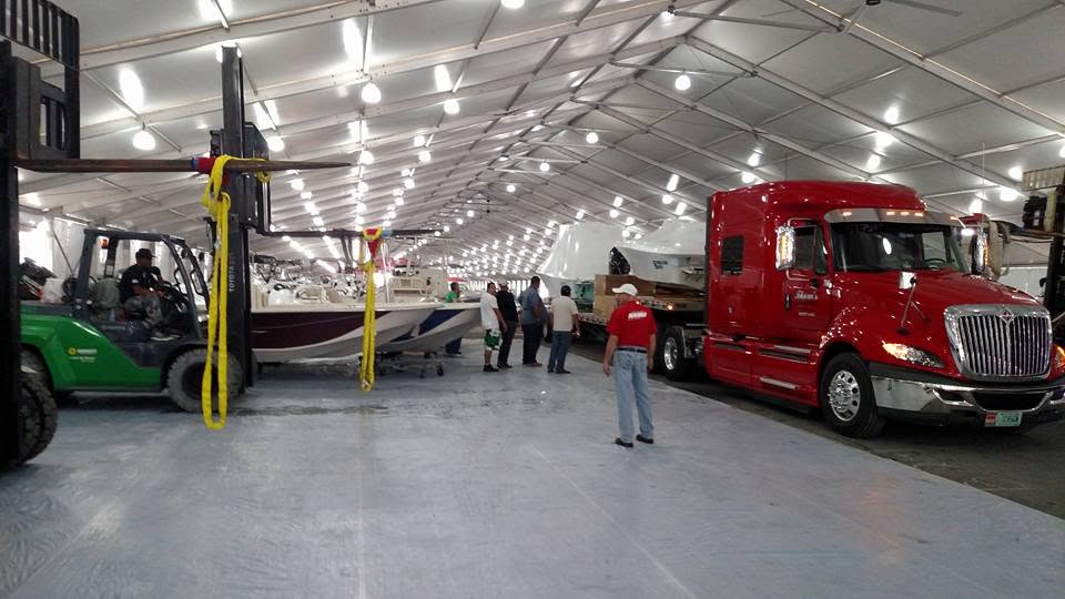 Boat-show load-in with transport truck, forklift, boats, and crew working on the exhibition floor